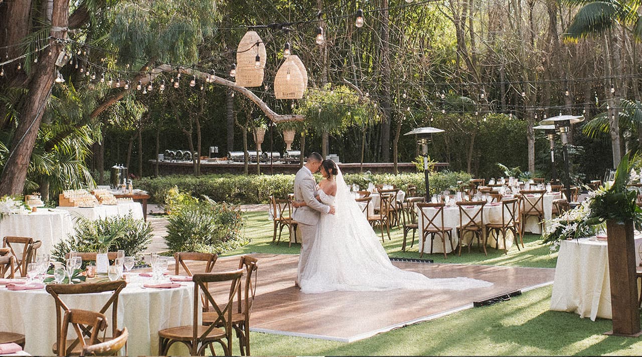Bride and groom sharing a romantic embrace on an outdoor wooden dance floor at a garden wedding reception.