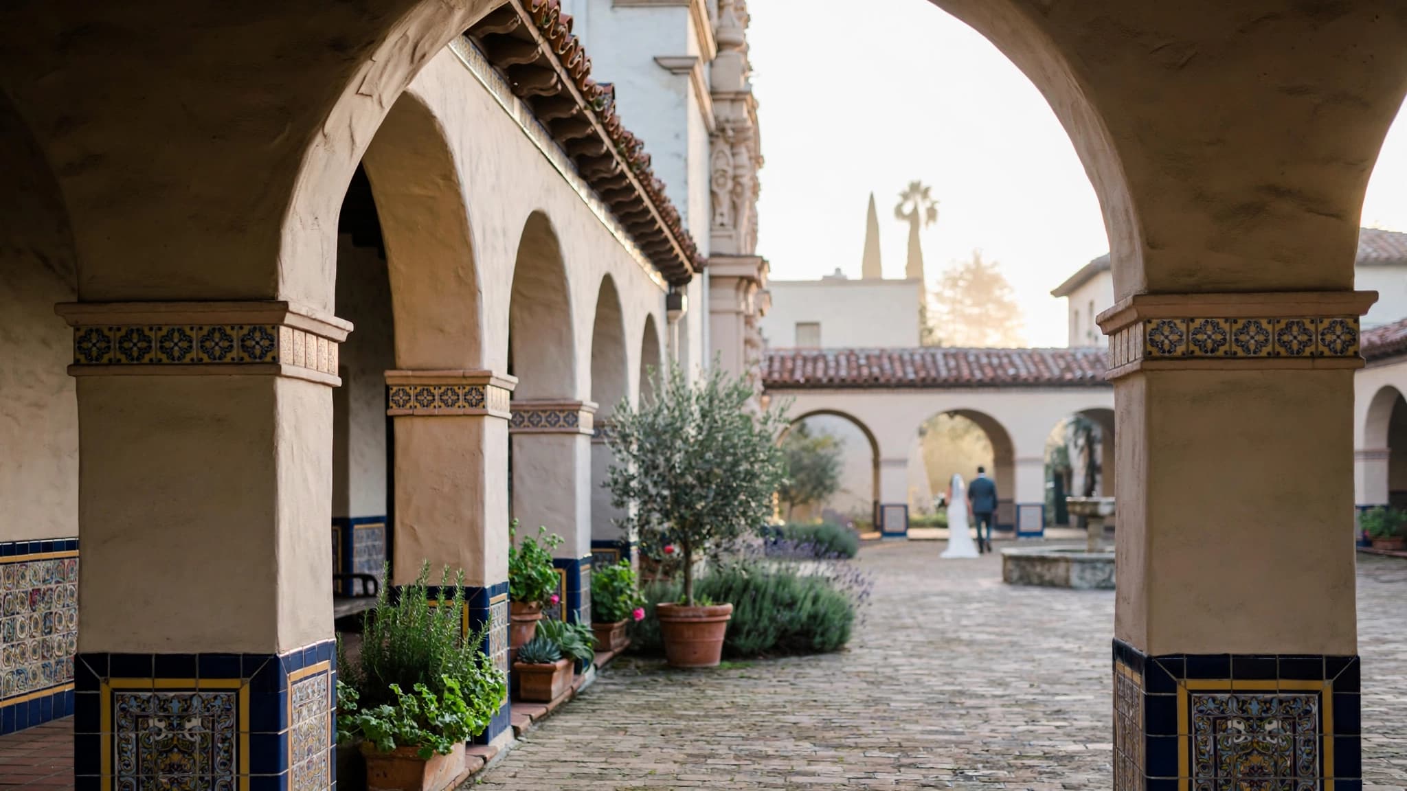 Santa Barbara Courthouse courtyard at sunrise, with arches and tilework in soft light and a couple walking in the distance